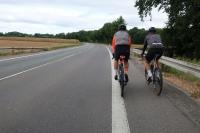 Zwei sportlich gekleidete Fahrradfahrer fahren eine Landstraße entlang